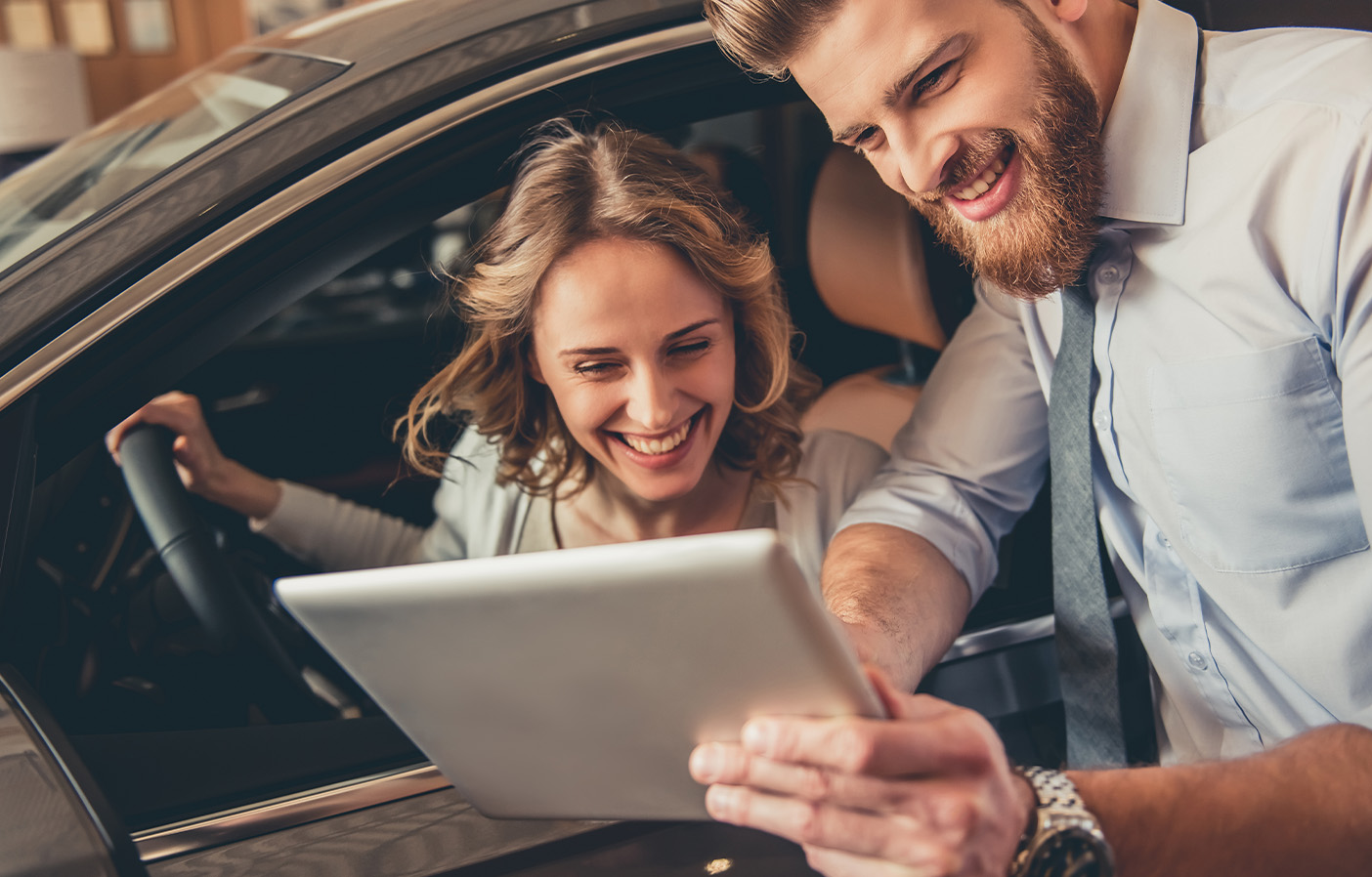 Dealership advisor and customer reviewing vehicle information on a tablet inside a car, representing automotive dealership services and customer support.