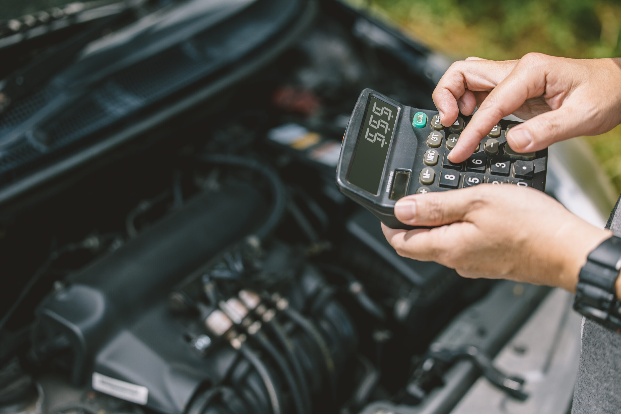 Closeup car owner calculate cost for service pay to fix a car with calculator against old car engine background