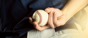 A baseball pitcher is holding his ball behind his back.