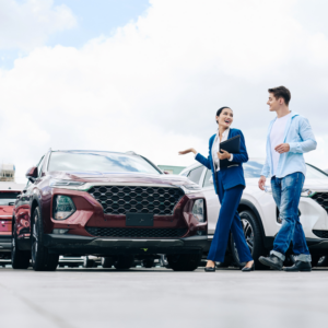 Car dealership saleswoman walking along rows of new cars with customer