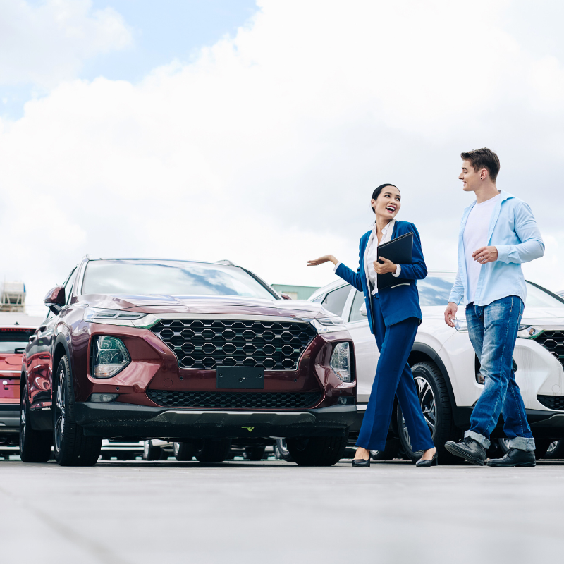 Car dealership saleswoman walking along rows of new cars with customer