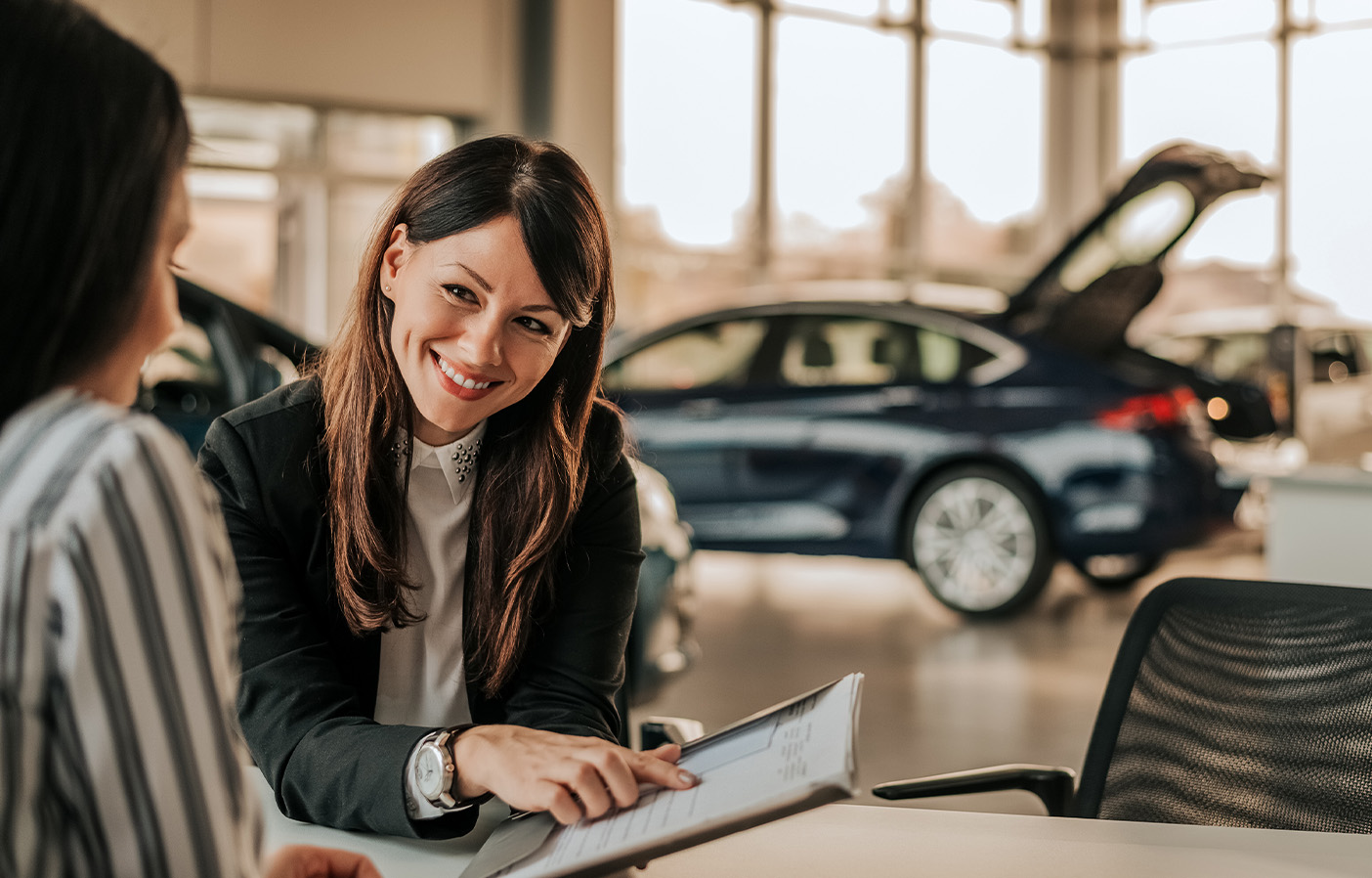 Dealership advisor reviewing financial documents with a client inside a car dealership showroom, representing outsourced accounting and financial services for automotive dealerships.