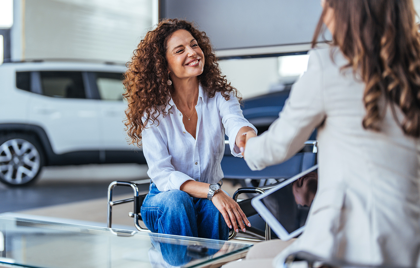 Two professionals shaking hands during a consultation inside an automotive dealership showroom, representing trusted advisory and dealership services.