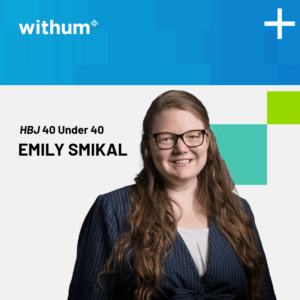 Emily Smikal is a middle-aged Caucasian woman smiling in a professional photo. She is wearing a black striped blazer and has long wavy red hair.