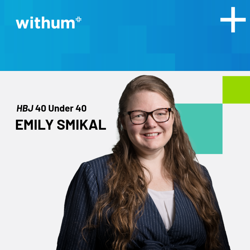 Emily Smikal is a middle-aged Caucasian woman smiling in a professional photo. She is wearing a black striped blazer and has long wavy red hair.