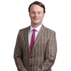 Profile headshot of Justin Bonk in a brown suit coat.
