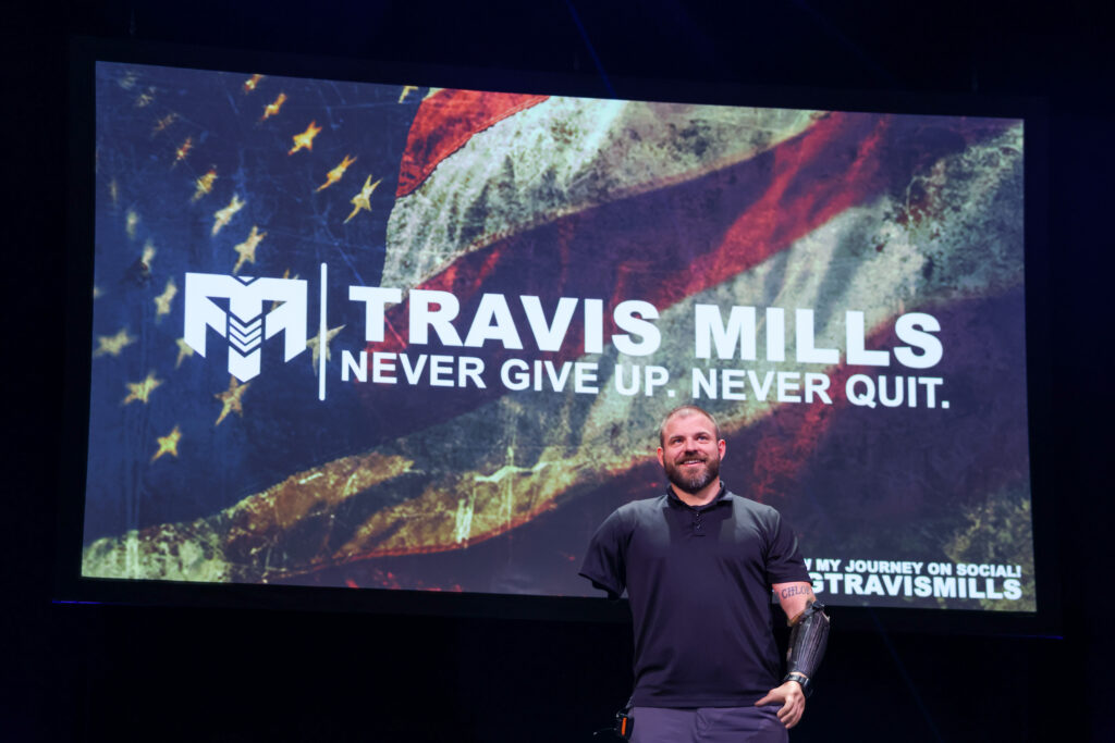 Travis Mills, State of the Firm speaker on stage smiling.