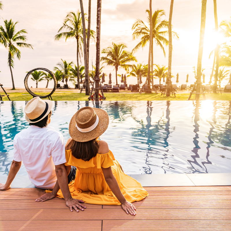 two hotel guests on vacation sitting by the pool watching the sunset.