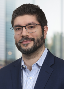 Matthew Magliano headshot in blue blazer and blue striped shirt.